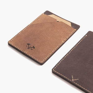Cropped image of two handmade leather card wallets in two shades of brown with hand stitching and etched logo detailing.