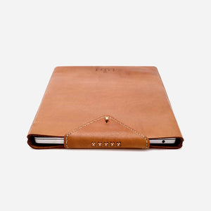 profile image of a camel brown leather laptop sleeve with a silver laptop inside. Leather laptop sleeve features white stitching and brass hardware details.