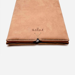 cropped image of a tan brown leather laptop sleeve with white and brown stitching and etched logo detailing.