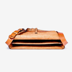 a caramel brown leather messenger style bag lying flat on a white surface, open wide so empty contents are visible. Bag has etched logo and stainless steel hardware details