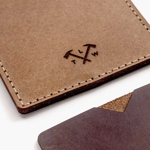 close cropped image of two handmade leather card wallets in two shades of brown with hand stitching and etched logo detailing.