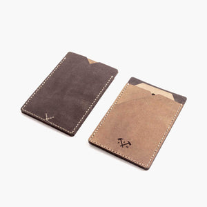 Two handmade leather card wallets lying flat on a white surface in two shades of brown with hand stitching and etched logo detailing.