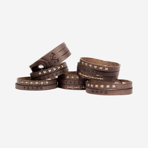 multiple stacks of dark brown leather wristbands with etched logo and type detailing as well as stitching details