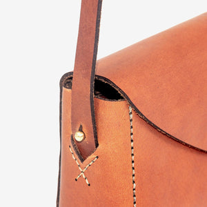 close up view of brown leather handbag featuring white stitching detail and brass hardware