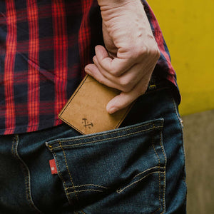  A person placing a natural brown leather card wallet into the back pocket of his jeans.