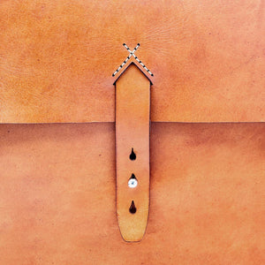 cropped image of a caramel brown leather messenger bag with white hand stitched details and a brass hardware closure.