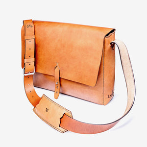 a caramel brown leather messenger style bag with a thick shoulder strap, stainless steel hardware, hand stitching and etched logo details.